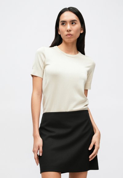 Bēša īsslēgta topiņa ar apaļu kakla izgriezumu, kombinēta ar melnu svārku. Audums izskatās gluds ar nelielu tekstūru uz krekla.