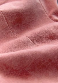 Soft pink fabric with a velvety texture, featuring subtle seams and a smooth, slightly glossy surface. Close-up view highlights details.