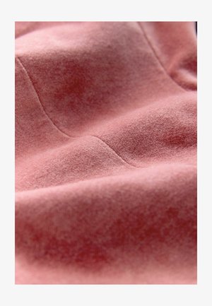 Soft pink fabric with a velvety texture, featuring subtle seams and a smooth, slightly glossy surface. Close-up view highlights details.