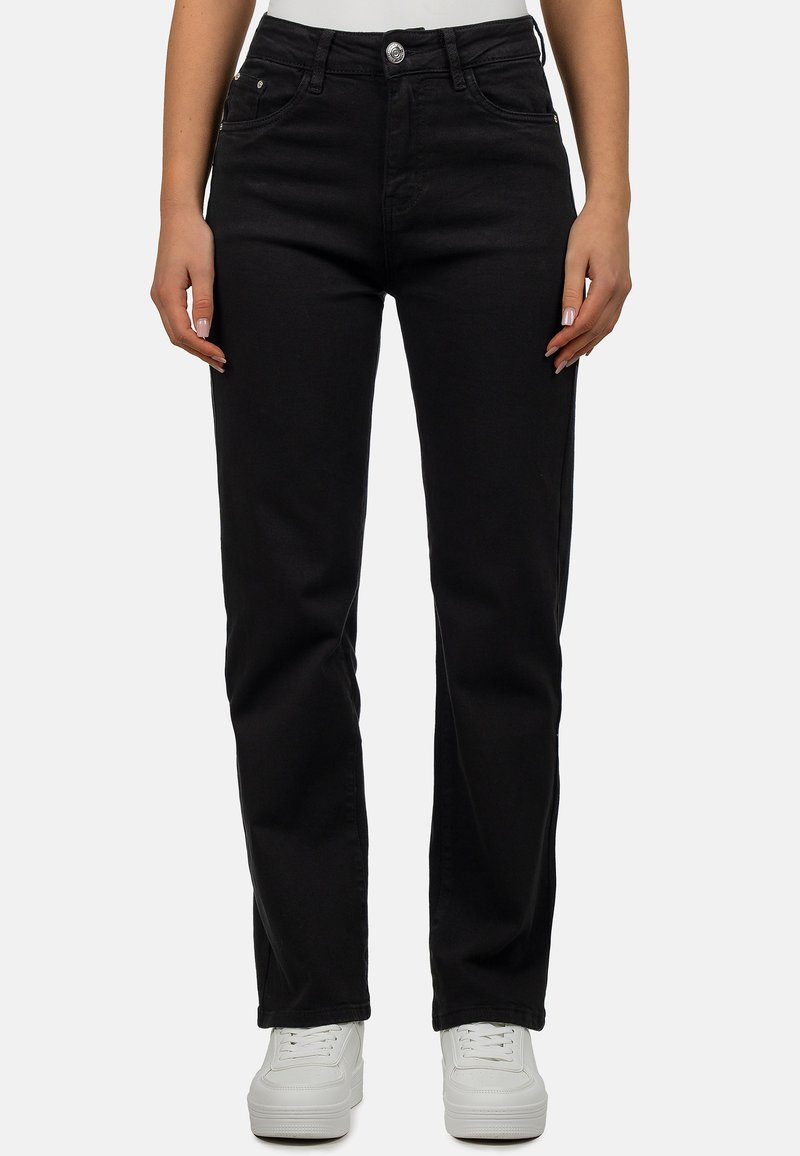 Jean en denim noir avec une coupe droite, design à cinq poches et fermeture à bouton en métal, associés à des baskets blanches.