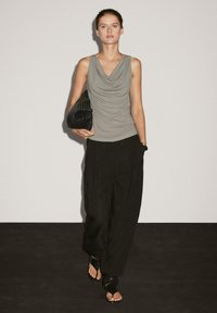Sleeveless, draped grey top; loose black trousers with a wide leg; carrying a textured black bag; flat black sandals. Minimal design.