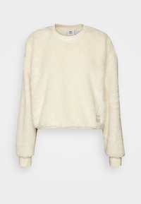 Krämfärgad kort sweatshirt med fluffig textur, rund halsringning och ribbade ärmmuddar. Har en liten logotyp på framsidan.