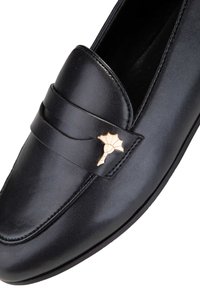 Svart läderloafersko med rund tå, utrustad med en dekorativ guldfärgad bladsmycke och en sydd kant längs ovandelen.
