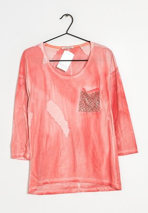 Haut manches longues de couleur corail avec encolure dégagée, poche appliquée texturée ornée de décorations, et coupe décontractée.