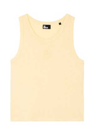 Jonge vrouw draagt een geel mouwloos topje, lichtblauwe wijde spijkerbroek, zwarte sandalen met bandjes en een bruine schoudertas.