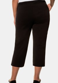 Zwarte cropped broek met een elastische tailleband, voorzien van een gladde textuur en rechte pijpen, die net boven de enkel eindigen.