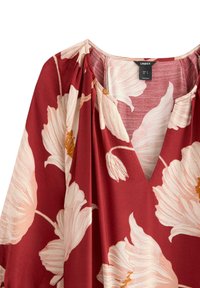 Röd blommig blus med V-ringning, som har vita och gyllene blommönster. Tillverkad av mjukt tyg, med lediga, flödande ärmar och en mjuk fall.
