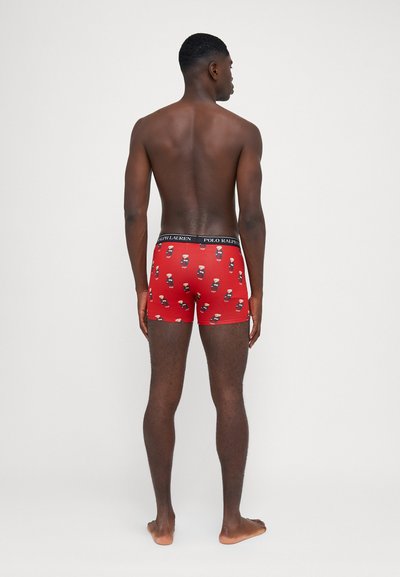 Boxer rouge avec un motif imprimé de petites figures, avec une taille noire portant le texte "POLO RALPH LAUREN." Conçu pour le confort.