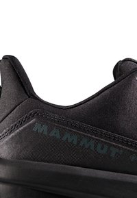 Sort stof sko med struktureret overdel, der har et fremtrædende "MAMMUT" logo, slank design, rund krave og forstærkede syninger.