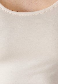 Top in maglia beige con scollo rotondo, caratterizzato da una texture in costina fine e dettagli di cucitura sottili lungo i bordi.