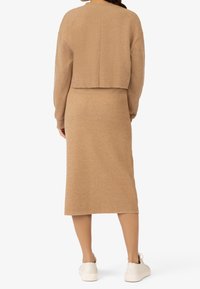 Pull beige raccourci à manches longues associé à une jupe midi de la même couleur, le tout dans un tissu doux et texturé. Des baskets blanches complètent le look.