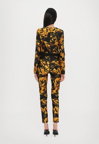 Black fabric outfit featuring an intricate yellow baroque pattern, consisting of a fitted long-sleeve top and slim pants, paired with high heels.