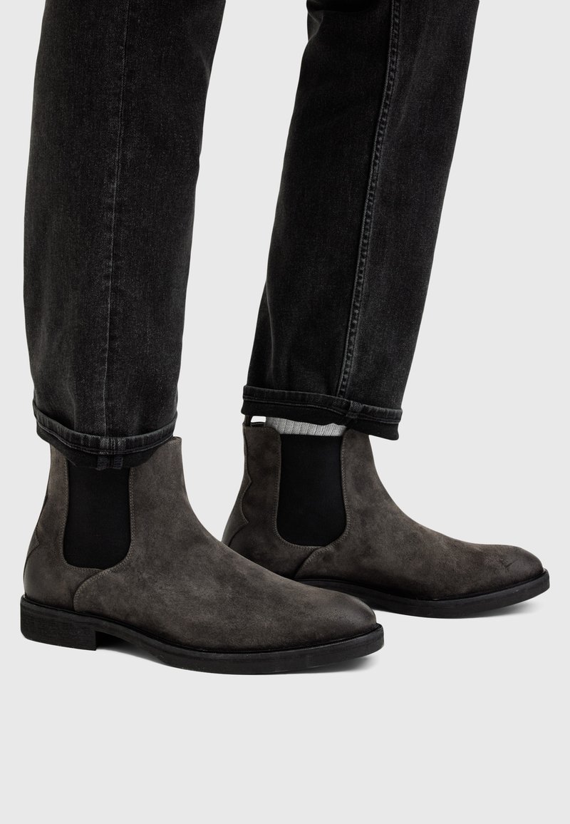 Botas Chelsea de ante gris con paneles laterales elásticos, punta redonda y suela de goma plana. Se combinan con un vaquero oscuro y un calcetín en contraste.