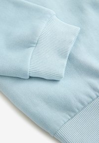 Primo piano di un tessuto di felpa blu chiaro, con polsini a coste e una texture liscia, che mette in evidenza i dettagli della cucitura e una finitura morbida.