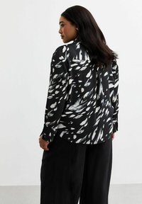 Zwart-witte gestreepte shirt van lichtgewicht stof, met lange mouwen, een puntige kraag en een gespleten achterkant.