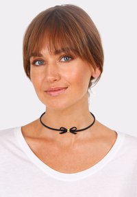 Schwarzes Choker aus Wildleder mit einem dünnen Band und einem kleinen Schleifendetail, das in der Mitte mit einem metallischen, goldenen Akzent verziert ist.