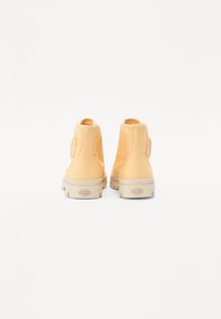 Boots de glezna galbene din pânză, cu o petică rotundă cu logo pe lateral, talpă de cauciuc bej și superior din țesătură texturată, prezentate din spate.