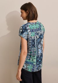 Blusa a maniche corte con design patchwork con motivi floreali blu, verde e bianchi, realizzata in tessuto leggero. Vestibilità rilassata.