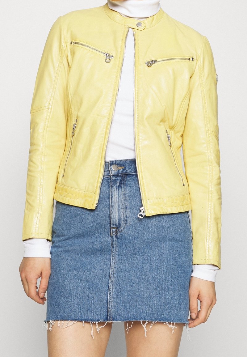 Giacca di pelle gialla con colletto rotondo, tasche con zip e taglio slim, abbinata a una gonna di jeans a vita alta con orlo sfilacciato.