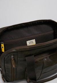 Braune Leder-Umhängetasche mit glatter Textur, ausgestattet mit einem Reißverschluss-Hauptfach, mehreren Taschen und einem gelben Akzent-Tag.