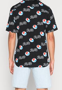 Black short-sleeve shirt featuring a repeating Pepsi logo pattern in red, white, and blue, made of lightweight fabric.