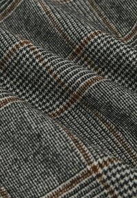 Vilnos audinys su juodai balta houndstooth rašto danga, pabrėžta rudos spalvos linijomis. Minkšta tekstūra; su raukšlėmis, parodydama gylį ir sluoksnius.