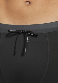 Męski tułów w czarnych szortach do biegania Nike z widocznym sznurkiem, związanym w kokardę poniżej pępka.
