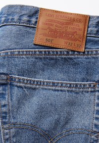 Blue denim jeans with a leather patch labeled "Levi Strauss & Co." featuring embossed design. Includes back pockets and contrasting stitching.