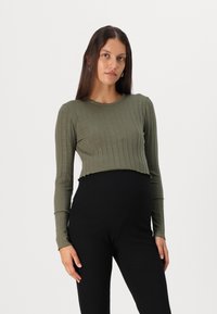 Oliivroheline, soonikute mustriga, lühendatud pika varrukaga pluus ümarate kaelus ja brutokäe äärega, kombinatsioonis mustade slim-fit pükstega.
