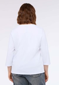 Maglietta bianca a maniche lunghe con scollatura rotonda, realizzata in tessuto leggero, abbinata a jeans in denim blu con taglio classico.