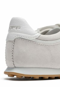 Baskets en daim gris clair avec accents en cuir blanc, dotées d'un talon arrondi, d'une surface texturée et d'une semelle extérieure en caoutchouc avec des crampons pour l'adhérence.