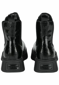 Botines de charol negros con una suela gruesa y texturizada y un detalle en la parte posterior con marca. Presentan un acabado suave y paneles laterales elásticos.
