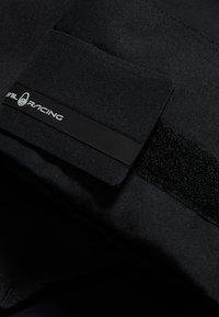 Sort tekstil med en blød tekstur, der har en velcro-lap og en sort rektangulær label med hvid "STL RACING" tekst.