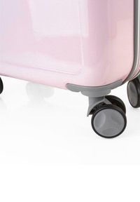 Maleta rígida rosa con superficie lisa, acentos grises y cuatro ruedas negras giratorias para una fácil movilidad. Notable brillo sutil.