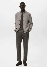 Beżowy sweter na guziki na brązową koszulę, do tego brązowe spodnie i ciemnobrązowe buty. Strój ma zapinaną na guziki przednią część i dopasowany fason.