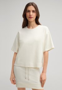 Cremfarbener, lässiger Sweatshirt mit kurzen Ärmeln, aus weichem Material. Kombiniert mit einem passenden Rock mit Kordelzugdetails.