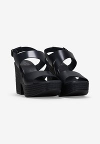 Sandalias de cuña negras con tiras entrelazadas, hechas de cuero suave. Plataforma y tacón texturizados. Correa ajustable en el tobillo con hebilla.