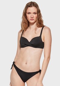 Conjunto de bikini negro que presenta un top bandeau retorcido con tirantes ajustables y una parte inferior de tiro bajo a juego con lazos laterales. Textura mate suave.