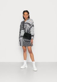 Vestido de camisa com padrão preto e branco, de mangas longas, combinado com uma mala preta texturizada e botas de cano curto brancas com amarração.