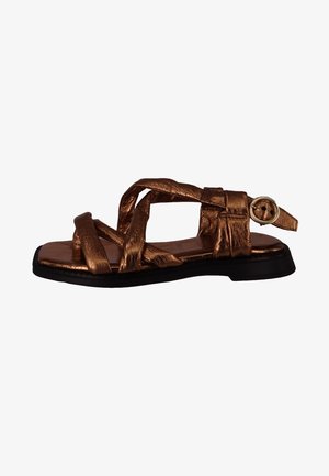 Bronze-colored sandal with woven straps, a flat black sole, and a round gold buckle accent on the ankle strap. Smooth texture throughout.
