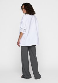 Sudadera blanca de gran tamaño con mangas enrolladas, combinada con pantalones gris holgados. Textura suave, diseño minimalista y sin patrones ni acentos visibles.