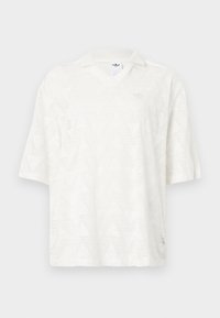 Λευκό πόλο μπλουζάκι με κοντά μανίκια, διακριτικό τριγωνικό μοτίβο, γιακά V και μικρό λογότυπο Adidas στο στήθος και στην ετικέτα μέσα στον γιακά.