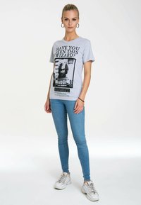 Gray cotton t-shirt featuring a black and white graphic print with the text “HAVE YOU SEEN THIS WIZARD?” paired with blue denim skinny jeans and white sneakers.