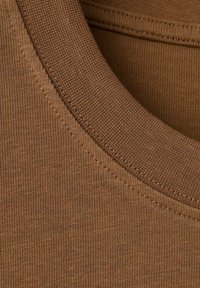 Brązowa bawełniana tkanina na koszulkę, zbliżenie, z okrągłym dekoltem i fakturowanym wzorem dzianiny oraz widocznym przeszyciem wokół kołnierza.