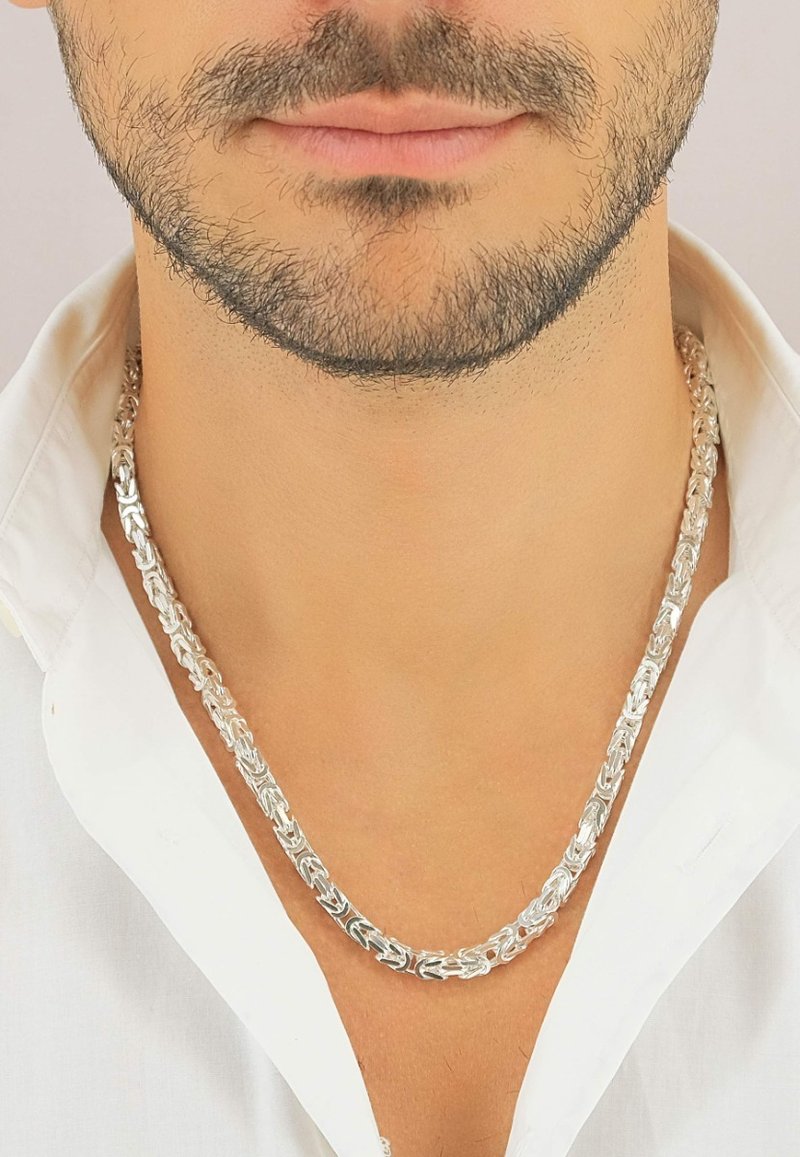 Collier en argent composé de maillons entrelacés, avec une finition lisse et une texture polie, porté sur une chemise blanche.