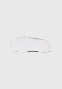 Semelle de basket blanche avec des motifs de traction texturés et un petit logo Puma sur le talon, sur un fond blanc uni.