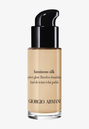 Luminous Silk foundation flaske, klar glass med svart pumpehette, lys beige væske, preget tekst med merke- og produktinformasjon.
