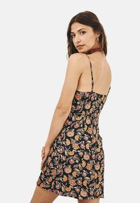 Vestido de patrón floral en negro con tirantes finos, corsé ajustado y dobladillo acampanado. Presenta motivos florales multicolores y una textura suave.