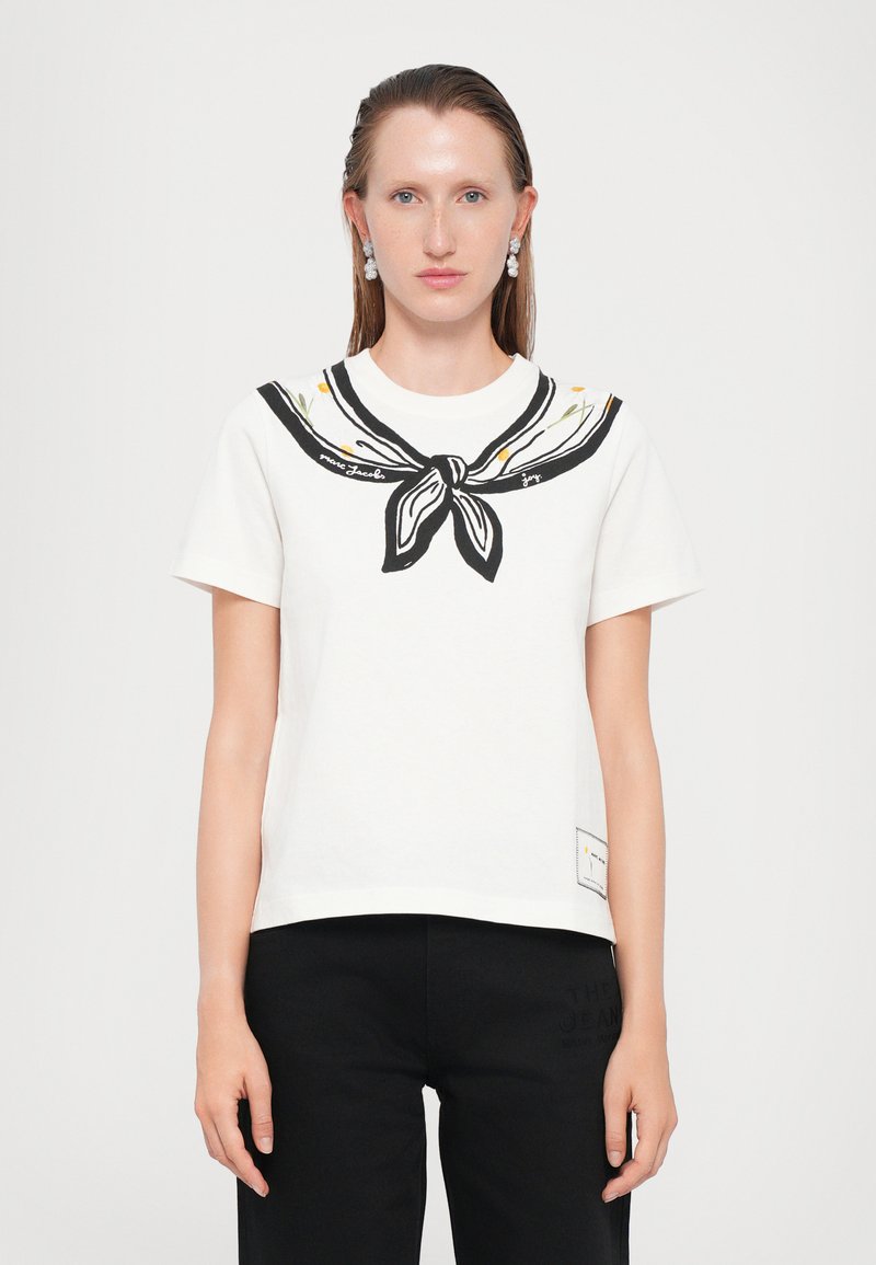 Tricou alb din bumbac cu un design de guler de marină negru, având accente florale și o etichetă în partea dreaptă jos. Mâneci scurte și croială lejeră.
