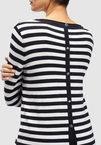 Pull à rayures noires et blanches avec un col rond et des boutons décoratifs le long de l'ouverture au dos. Tissu en maille douce, manches longues.